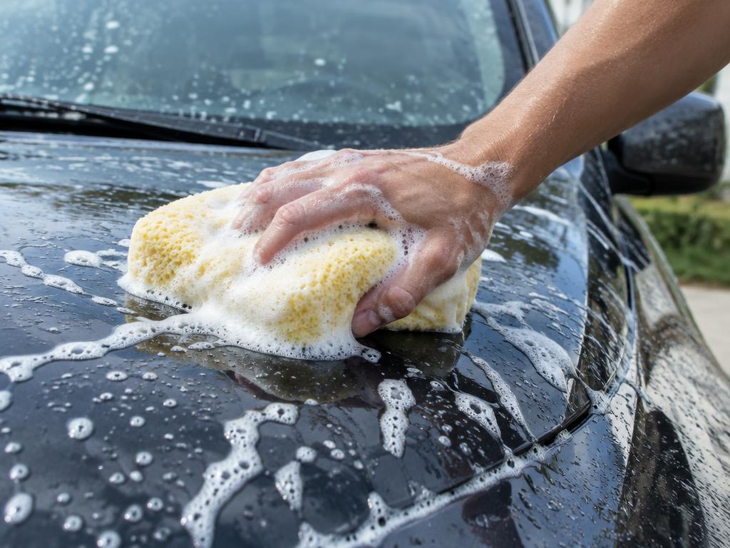 Mão com esponja e espuma a lavar o capô de um automóvel
